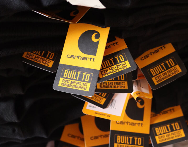 An image of stacked Carhartt® CTK87 Workwear Pocket Short Sleeve T-Shirt hang tags highlighting branding details and product specifications