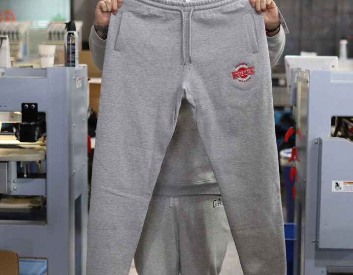 A person holding up a pair of grey sweatpants in an industrial workspace.