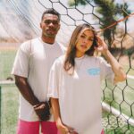 Two individuals standing confidently behind a soccer goal net, dressed in Custom Printed Heavyweight Cotton T Shirts.