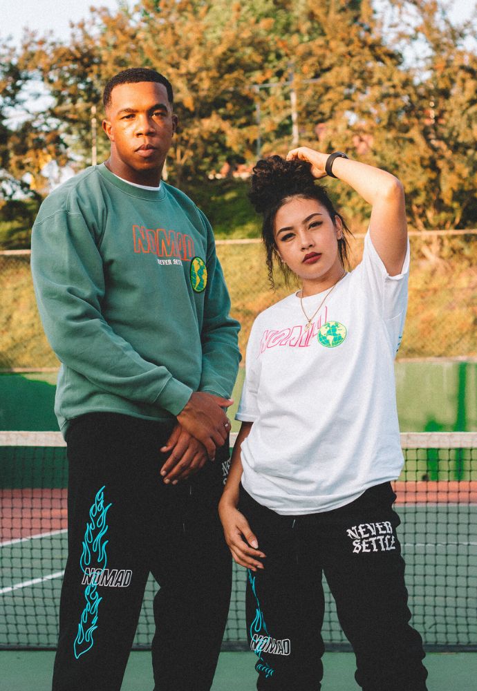 Two individuals posing in casual streetwear on a tennis court.