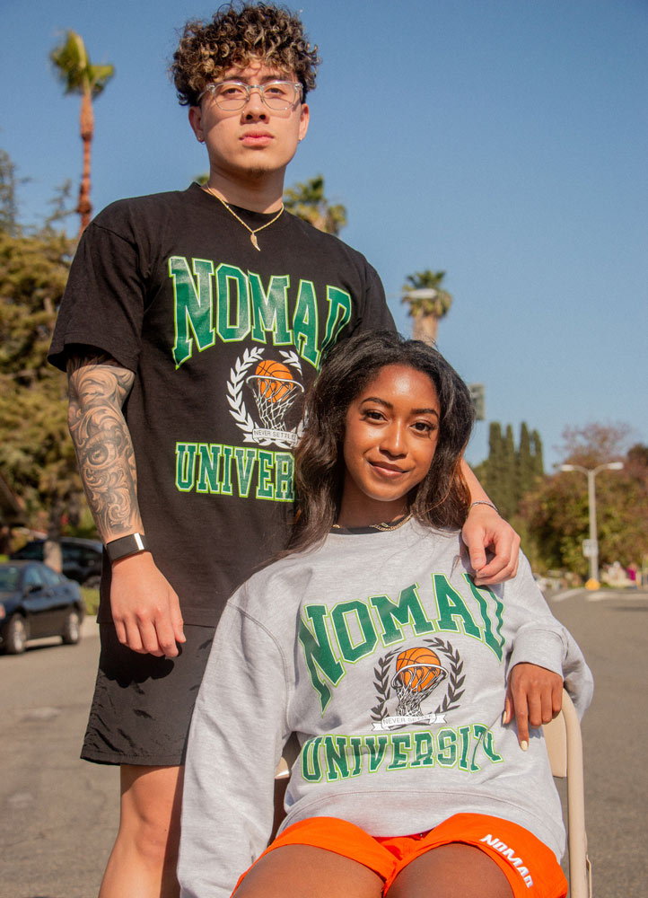 Two individuals posing for the camera on a sunny day, wearing sporty 'nomad university' apparel.
