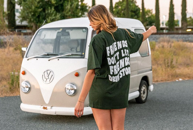 Woman in a t-shirt with text standing near a vintage volkswagen van.