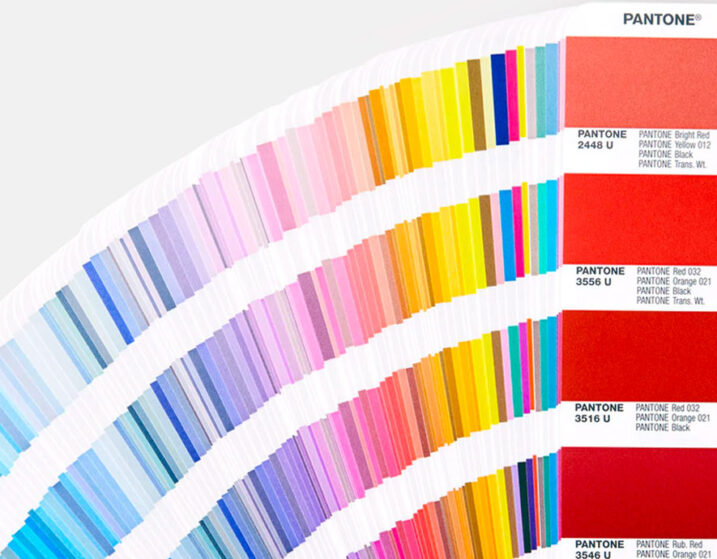 A fan of Pantone color swatches displaying a gradient range of hues from cool to warm tones, with specific color codes and names listed on each swatch, perfect for selecting colors for custom screen printing and embroidery services.