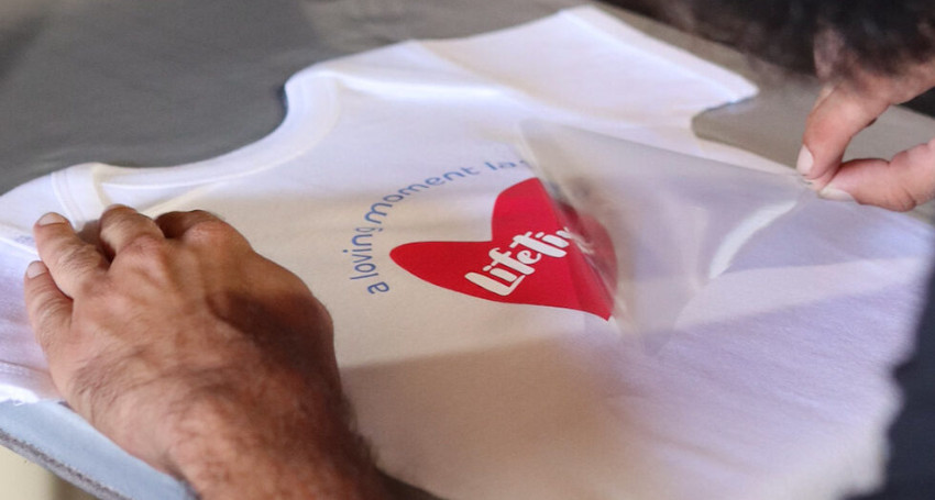 A person applies a red and white branded heat transfer graphic onto a white t-shirt, discovering types of print.