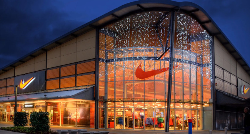 Exterior of a Nike store at twilight, decorated with sparkling string lights, showcasing polo shirts and footwear through the large glass front.