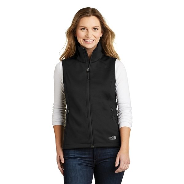 A woman with long hair wearing a white long-sleeve shirt and a black Women's The North Face Vest stands smiling against a white background. The vest features a small logo on the bottom left side.