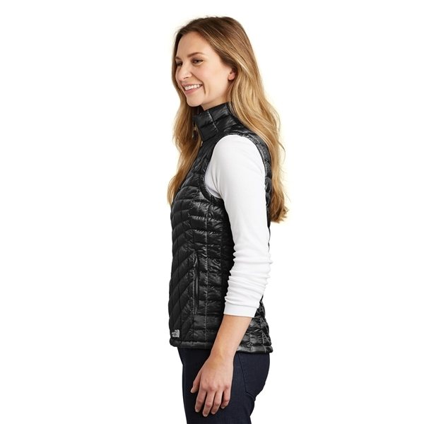 A woman with long hair is standing sideways, smiling, and wearing a Women's The North Face Vest in black quilted fabric over a white long-sleeve shirt.
