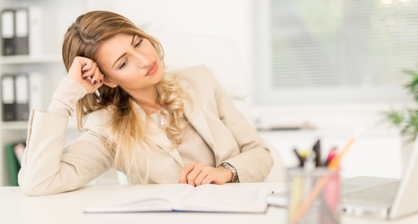 A woman in a beige suit looks tired as she leans her head on her hand at an office desk with a laptop and notebook, discovering types of print.