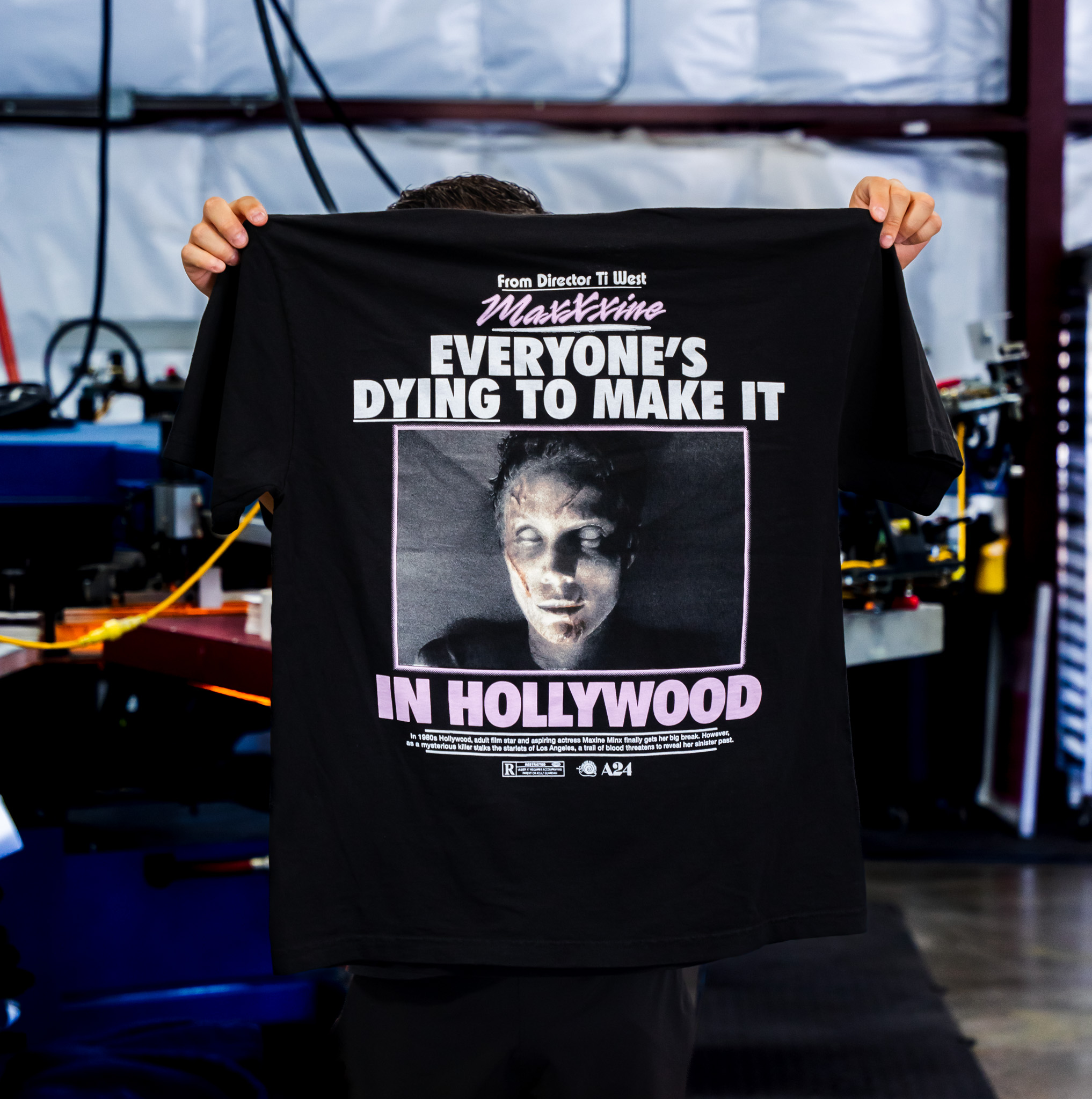 A man holding the Los Angeles Apparel 1801GD 6.5oz Garment Dye Crew Neck T-Shirt in Black with Custom Jumbo Screen Print with Maxxine design for movie merch printed by Garment Decor back view