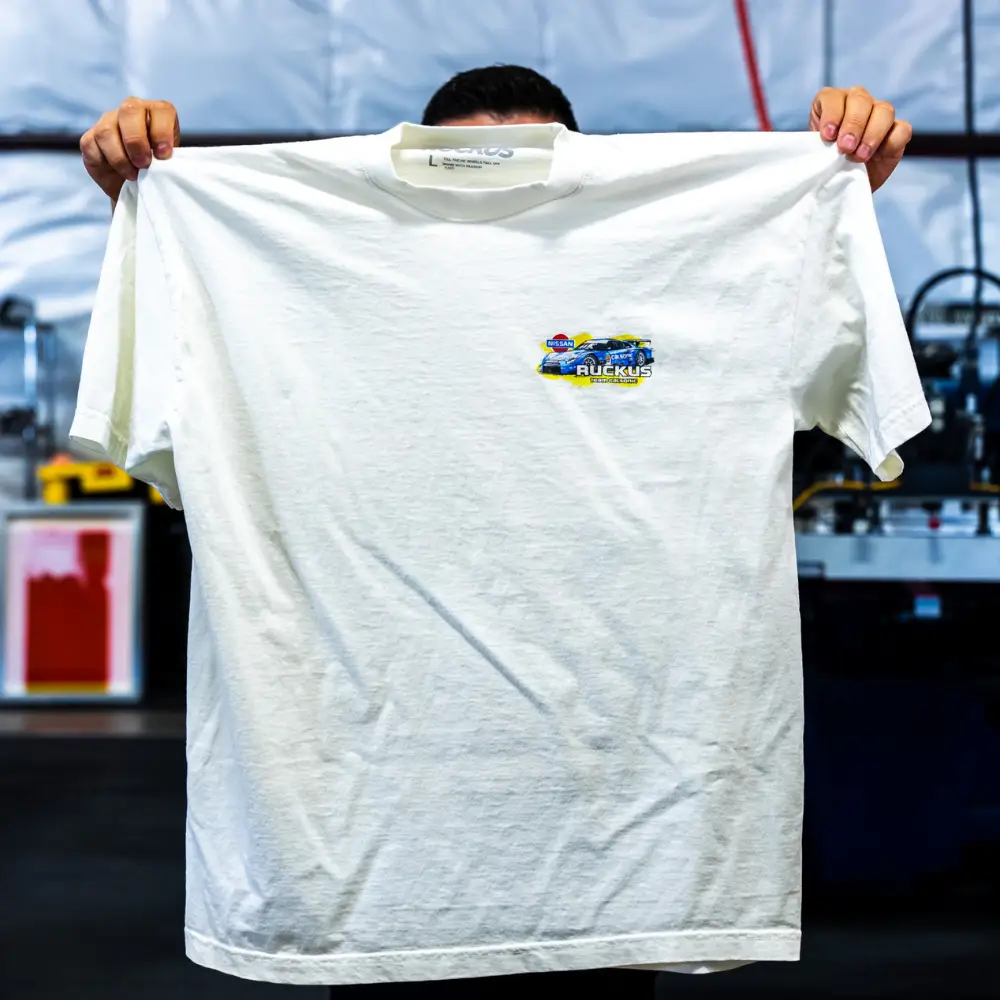 A man holding the front view of a white Los Angeles Apparel 1801GD 6.5oz Garment Dye Crew Neck T-Shirt featuring detailed digital squeegee printing of Garment Decor