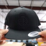 This is a photo of a black Flexift 6089M snapback hat with custom tonal 3d puff embroidery.